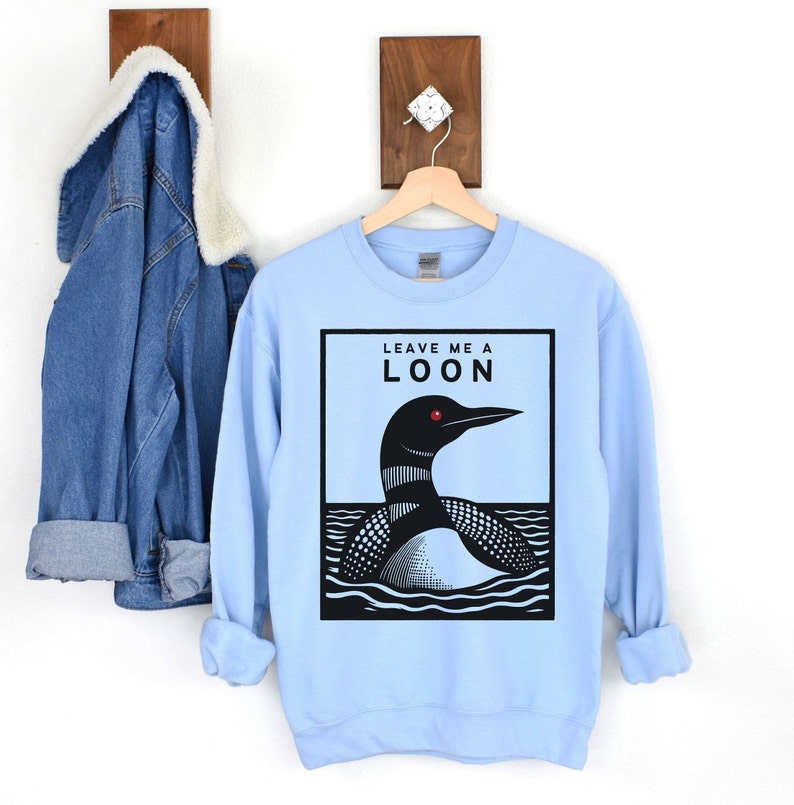 May include: Light blue sweatshirt with a black and white illustration of a loon on the front. The text "Leave me a loon" is printed above the loon.