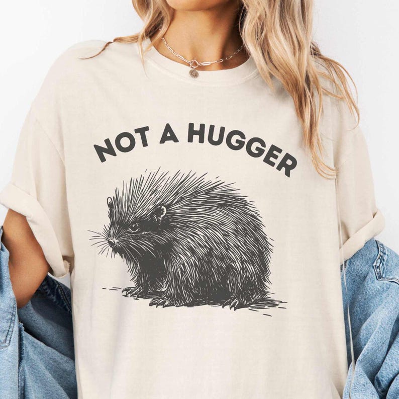 May include: A beige t-shirt with a black and white illustration of a hedgehog and the text "Not a Hugger".