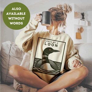 May include: A cream-colored sweatshirt with the text "Leave me a loon" and a black and white illustration of a loon. The sweatshirt is available without the words.
