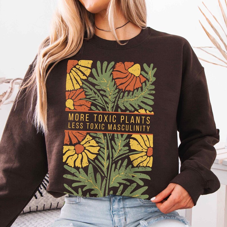 May include: Brown sweatshirt with a floral design and the text "More Toxic Plants Less Toxic Masculinity".