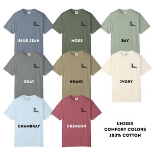 May include: A collection of unisex Comfort Colors t-shirts in various shades, including blue jean, moss, gray, khaki, ivory, chambray, and crimson. Each shirt features a small embroidered design and is made of 100% cotton.