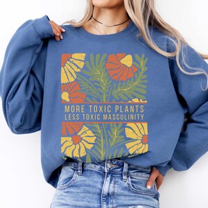 May include: A blue sweatshirt with a floral design and the text "More Toxic Plants Less Toxic Masculinity".