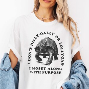 May include: White t-shirt with a black and white illustration of a turtle and the text "I don't dilly-dally or lollygag I mosey along with purpose."
