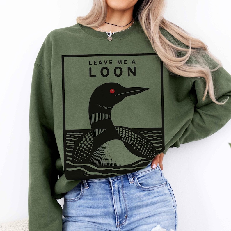 May include: A green sweatshirt with a black and white graphic of a loon on it. The graphic says "Leave Me A Loon".
