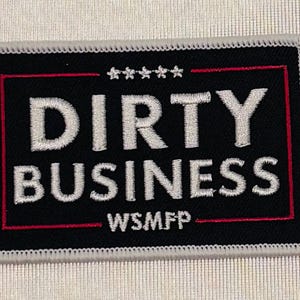May include: A rectangular embroidered patch with a black background and a white border. The text DIRTY BUSINESS is embroidered in white capital letters. Above the text are five white stars, and below is the white text WSMFP, all enclosed in a thin red rectangular frame.