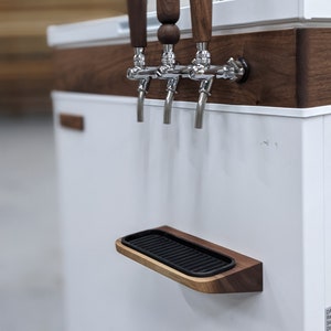 May include: A white beverage dispenser with a walnut wood trim and three wooden beer taps. The dispenser has a black drip tray.