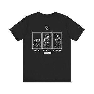 May include: Black t-shirt with a graphic design showing three panels. The panels depict a figure falling, getting up, and standing with a sword. Text reads "FALL. GET UP. REPEAT. PROVERBS 24:16."