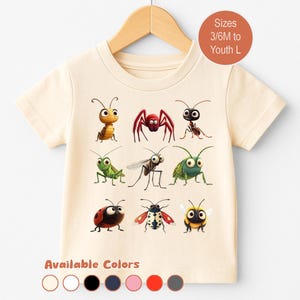 May include: Cream-colored t-shirt featuring a colorful insect graphic. The design includes a variety of cartoon bugs, such as a spider, ladybug, and bee. The shirt is displayed on a wooden hanger. Text on the shirt reads "Sizes 3/6M to Youth L".