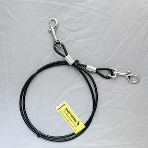 May include: Black dog tether with two silver-colored clips. The tether has a loop at each end and a central section with a metal sleeve. A yellow tag with the text "Tether Your Dog" is attached.
