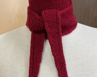 May include: A knitted burgundy scarf with long, dangling ends. The scarf is wrapped around a mannequin's neck, showcasing its texture and design. The scarf is a deep red color, perfect for adding warmth and style.