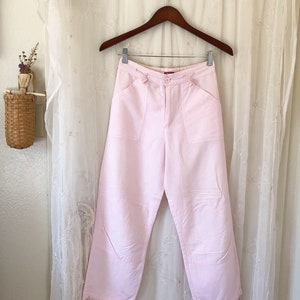 May include: A pair of light pink, wide-leg pants with pockets and a button closure.