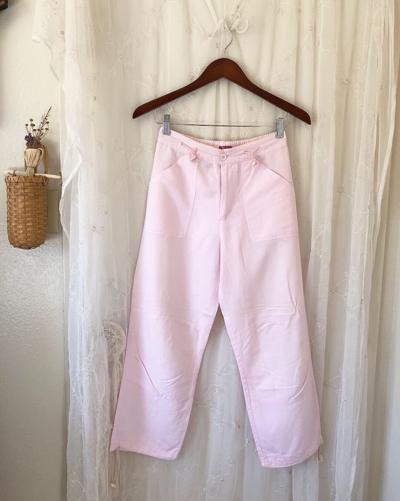 May include: A pair of light pink, wide-leg pants with pockets and a button closure.