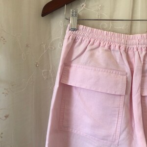 May include: Pink cotton pants with a drawstring waist and a large patch pocket on the back.