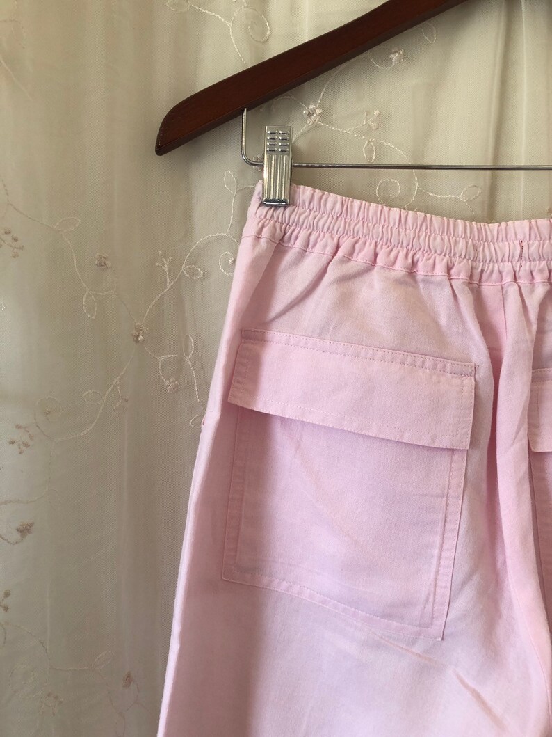 May include: Pink cotton pants with a drawstring waist and a large patch pocket on the back.