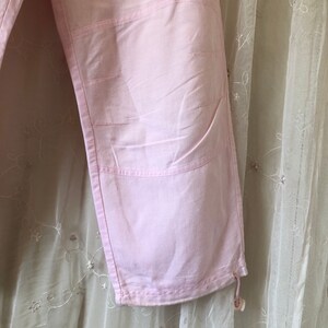 May include: A pair of pink pants with a drawstring at the bottom. The pants have a unique design with multiple seams and pockets.