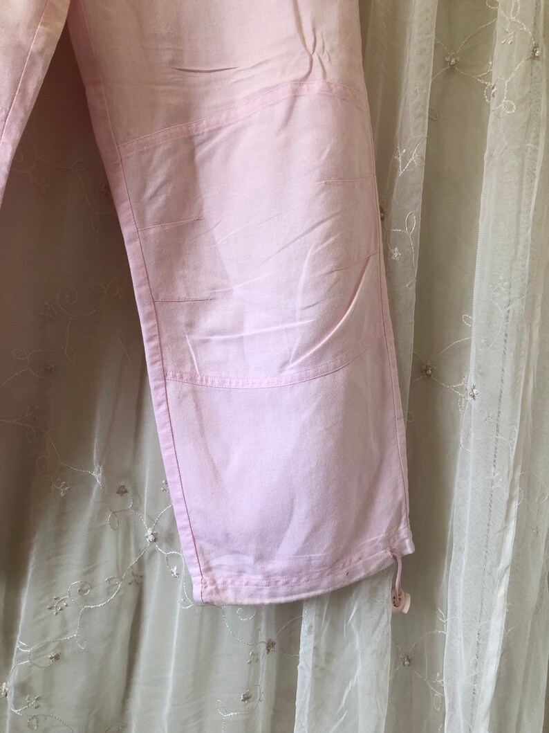 May include: A pair of pink pants with a drawstring at the bottom. The pants have a unique design with multiple seams and pockets.