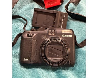 Cámara digital Canon PowerShot G12 de 10 MP, color negro, con zoom óptico de 5x, pantalla LCD de ángulo variable y cargador.