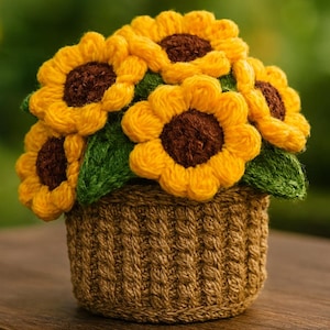Op de afbeelding: Een handgemaakt gehaakt zonnebloemarrangement in een kleine geweven mand. De zonnebloemen hebben heldergele bloemblaadjes en bruine centra, met groene bladeren. De mand is lichtbruin van kleur.