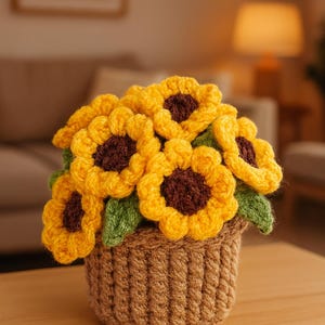 May include: A handcrafted crochet sunflower arrangement in a woven basket. The sunflowers have bright yellow petals and brown centers, with green leaves. The basket is a light brown color, and the arrangement sits on a wooden surface.