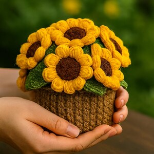 May include: A handcrafted crochet sunflower arrangement. The sunflowers have yellow petals and brown centers, set in a brown woven basket. The arrangement is held in a person's hands, with a blurred green background.