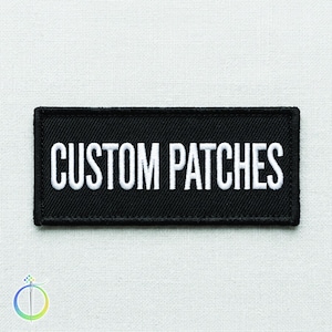 Könnte beinhalten: Ein rechteckiger schwarzer Aufnäher mit dem weißen gestickten Text "CUSTOM PATCHES". Der Aufnäher hat einen schwarzen Rand und wird auf einem weißen Stoffhintergrund angezeigt. Der Aufnäher ist wahrscheinlich für Kleidung oder Accessoires.