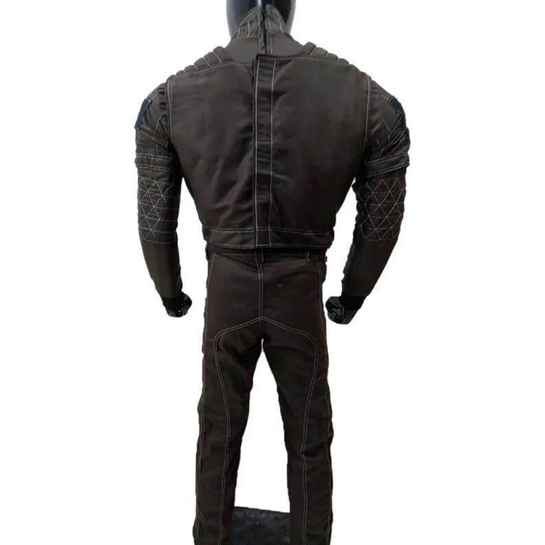 Op de afbeelding: Bruin jumpsuit met witte stiksels en gewatteerde details op de schouders en mouwen. Het pak heeft een hoge kraag en een rits op de rug. De mannequin draagt zwarte handschoenen.