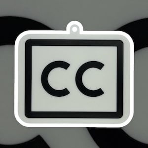 May include: A white, square-shaped keychain with a black border and the letters "CC" in bold black font. The keychain has a small loop at the top for attachment.