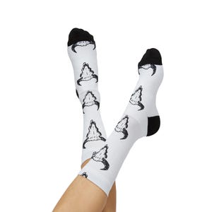 Könnte beinhalten: Weiße Socken mit schwarzen Akzenten an Zehen und Ferse. Die Socken zeigen ein sich wiederholendes Muster eines schwarz-weißen Schädeldesigns. Die Socken werden mit gekreuzten Füßen gezeigt.