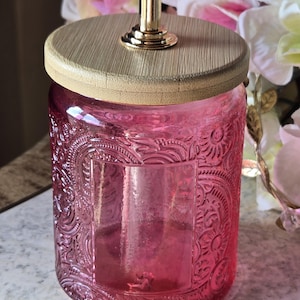 Tarro de cristal rosa con tapa de bambú y pomo de cristal en forma de corazón.