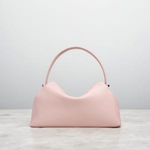 Puede incluir: Un bolso de mano rosa claro con un asa curva. El bolso tiene un cuerpo rectangular con un dise&ntilde;o superior &uacute;nico en forma de ola. El asa es de color rosa claro a juego, y el bolso parece estar hecho de un material texturizado.