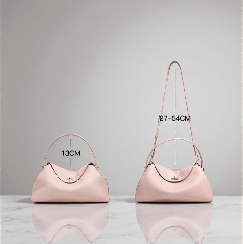 Puede incluir: Dos bolsos de mano de cuero rosa claro. Uno tiene un asa superior y mide 13 cm de ancho. El otro tiene una bandolera y mide 27-54 cm de alto. Ambos bolsos tienen forma curva y un peque&ntilde;o cierre met&aacute;lico.