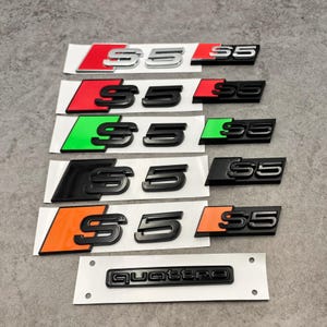 May include: A collection of S5 car emblems in various color schemes, including red, green, black, and orange. The emblems are black with a silver or colored background. A black Quattro emblem is also included.