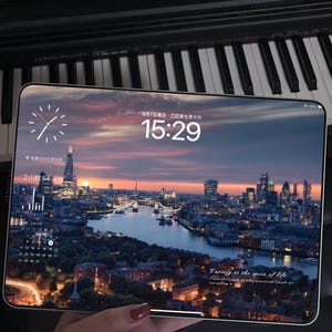 Könnte beinhalten: Ein Tablet, das eine Stadtlandschaft in der Abenddämmerung zeigt, wird vor einer Klaviertastatur gehalten. Der Bildschirm zeigt eine Uhr, Datum und Uhrzeit: 15:29. Das Bild enthält den Text "Variety is the spice of life."