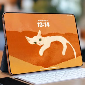 Könnte beinhalten: Ein goldfarbenes Tablet zeigt eine Illustration einer weißen Katze vor orangefarbenem Hintergrund. Die Uhrzeit 13:14 und das Datum Montag, 20. Mai sind zu sehen. Eine weiße Tastatur und ein schwarzes Smartphone sind im Vordergrund.
