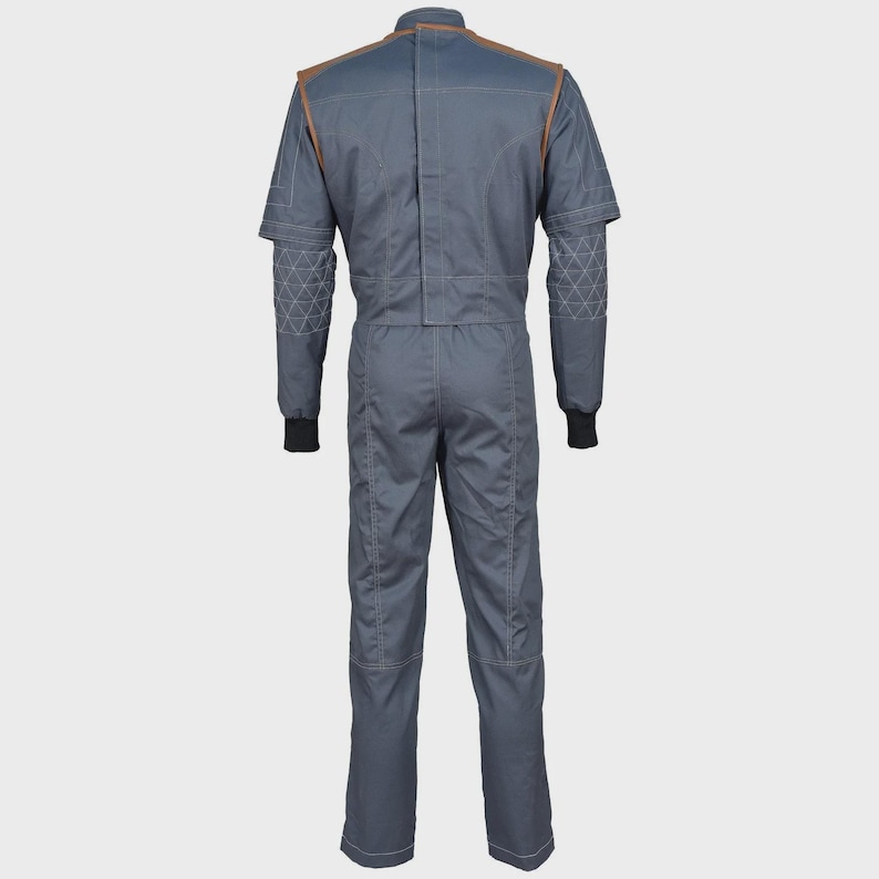 May include: A slate gray jumpsuit featuring a high collar, brown shoulder accents, and long sleeves with black ribbed cuffs. The forearms display a white geometric triangle pattern, while the back includes vertical seam detailing and a central closure.