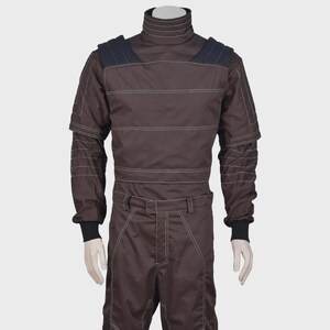 K&ouml;nnte beinhalten: Ein dunkelbrauner Langarm-Jumpsuit mit hohem Stehkragen, schwarzen Schulterpartien mit horizontalen N&auml;hten und wei&szlig;en Kontrastn&auml;hten. Das Kleidungsst&uuml;ck verf&uuml;gt &uuml;ber schwarze Rippb&uuml;ndchen an den &Auml;rmeln und einen passenden G&uuml;rtel in der Taille.