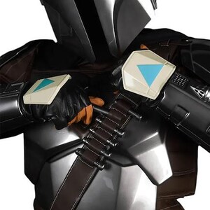 May include: A costume featuring a metallic silver helmet with a black visor, a chest plate, and dark brown fabric elements. The outfit includes a brown bandolier with silver cylindrical cartridges and black gloves with white and blue accents.