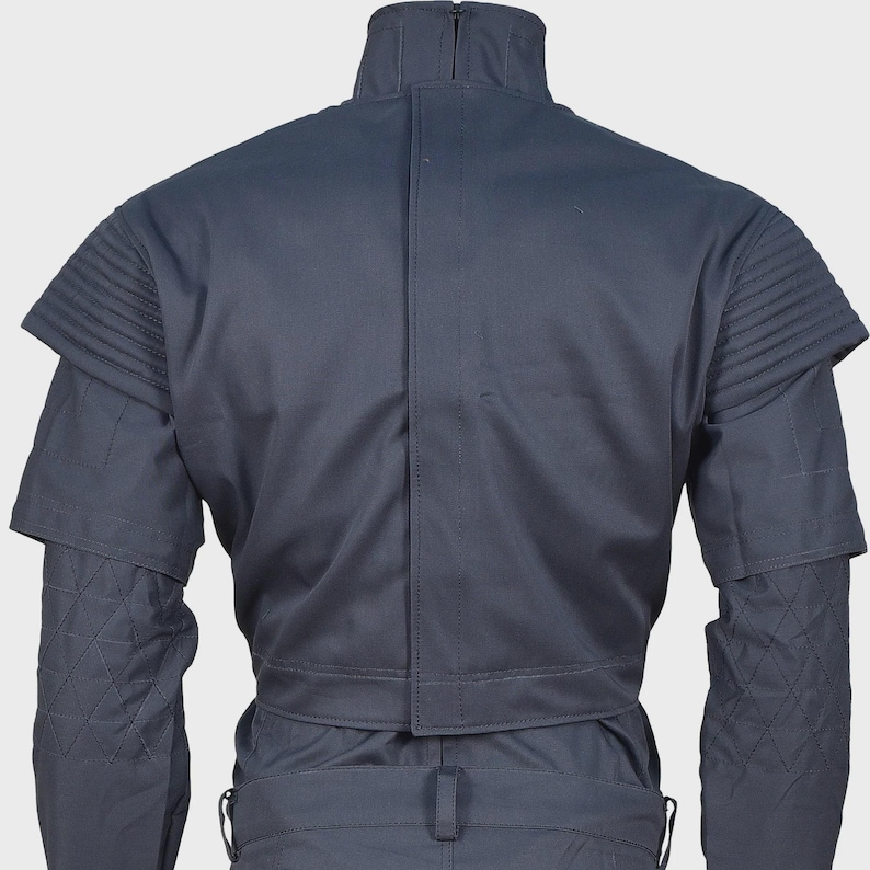 Peut inclure: Une veste gris fonc&eacute; dot&eacute;e d'un col montant, d'une fermeture centrale verticale et de panneaux d'&eacute;paules pliss&eacute;s. Les manches pr&eacute;sentent un motif en losanges matelass&eacute; sur la partie inf&eacute;rieure, avec une conception structur&eacute;e et uniforme.