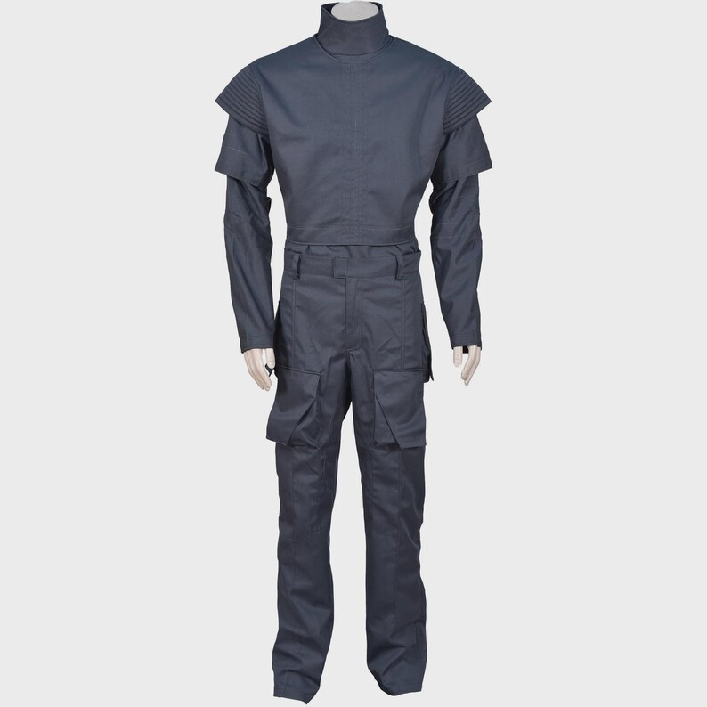Peut inclure: Une combinaison gris fonc&eacute; dot&eacute;e d'un col montant, de manches longues avec des d&eacute;tails c&ocirc;tel&eacute;s aux &eacute;paules et d'un corsage ajust&eacute;. Le pantalon comprend deux grandes poches cargo sur les cuisses et une ceinture structur&eacute;e avec passants.