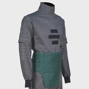 May include: A charcoal gray long-sleeve shirt featuring a high collar, white geometric line stitching on the sleeves, and three black rectangular patches on the chest. A dark green padded waist guard with horizontal stitching is worn over the shirt.