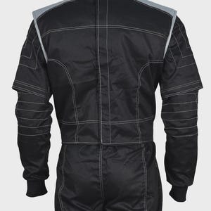 Puede incluir: Un traje de carreras negro con cuello alto, mangas largas con pu&ntilde;os acanalados y ribetes gris claro en los hombros. La prenda presenta costuras blancas visibles en toda su estructura, incluyendo l&iacute;neas horizontales en las mangas y el torso.