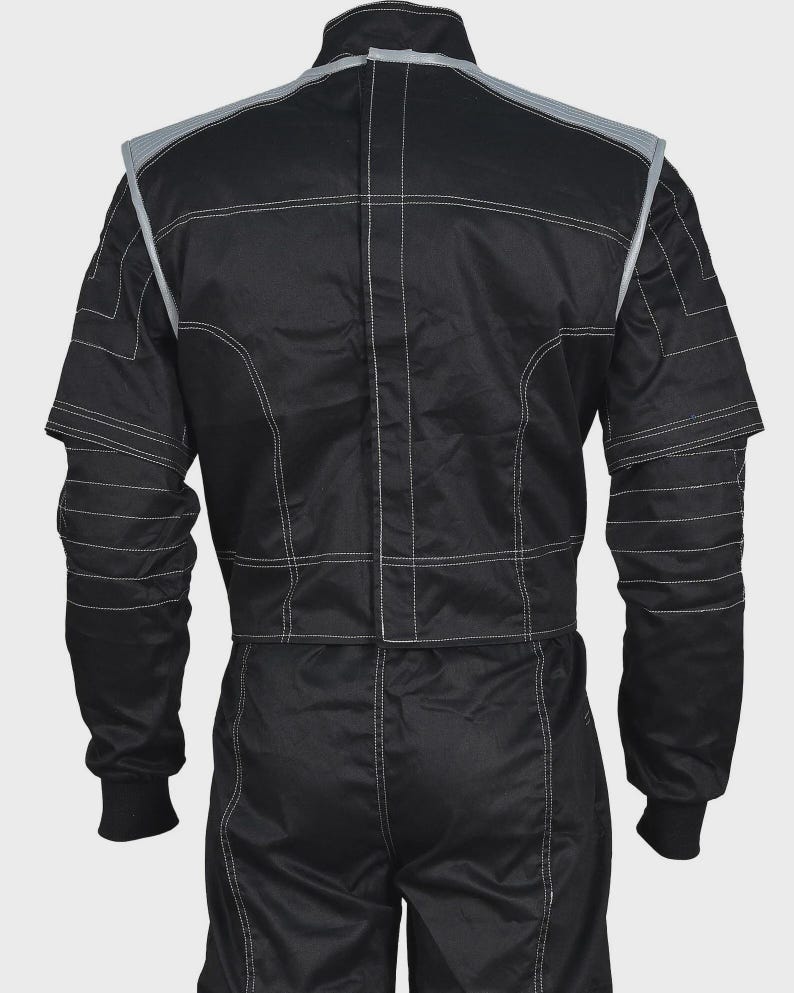 Puede incluir: Un traje de carreras negro con cuello alto, mangas largas con pu&ntilde;os acanalados y ribetes gris claro en los hombros. La prenda presenta costuras blancas visibles en toda su estructura, incluyendo l&iacute;neas horizontales en las mangas y el torso.