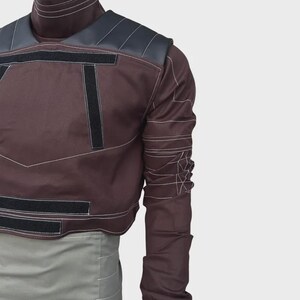 Puede incluir: Una camisa de manga larga color granate oscuro con cuello alto, paneles negros en los hombros y tiras de velcro negras en el pecho y la cintura. La prenda incluye costuras blancas en contraste a lo largo de todas las mangas.