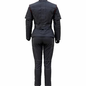 May include: A dark charcoal grey two-piece outfit consisting of a structured jacket and matching trousers. The jacket features a high collar, short sleeves with layered detailing, and a belted waist. Both pieces have prominent white topstitching.