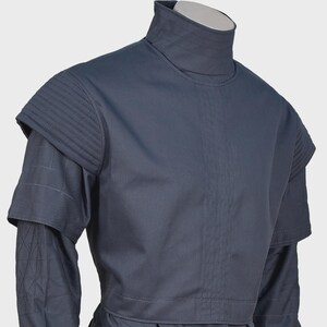 Peut inclure: Une tunique gris fonc&eacute; &agrave; col montant dot&eacute;e d'&eacute;paulettes structur&eacute;es avec des coutures horizontales, un panneau central vertical et des manches longues avec un motif en losanges matelass&eacute; sur les avant-bras. Finition mate uniforme.