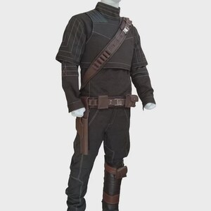 May include: A black long-sleeved shirt and matching pants set featuring white contrast stitching, a high collar, and a brown leather-like utility belt with a holster, a shoulder strap, and a matching brown leather-like leg guard on the lower right leg.