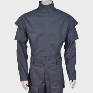 Peut inclure: Un haut &agrave; manches longues gris fonc&eacute; avec un col montant et des d&eacute;tails pliss&eacute;s aux &eacute;paules. Le v&ecirc;tement pr&eacute;sente un corsage structur&eacute; avec une couture horizontale au milieu et des manches longues, pr&eacute;sent&eacute; sur un torse de mannequin.