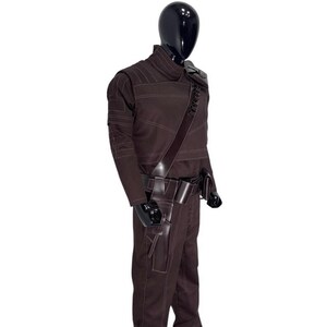 Peut inclure: Un ensemble veste &agrave; manches longues et pantalon marron fonc&eacute; avec des surpiq&ucirc;res claires. La tenue comprend une bandouli&egrave;re en similicuir marron fonc&eacute; avec des boucles int&eacute;gr&eacute;es, une ceinture utilitaire avec un &eacute;tui et une pochette.