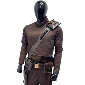 Peut inclure: Une tunique &agrave; manches longues et un pantalon assorti de couleur marron fonc&eacute; port&eacute;s par un mannequin noir. La tenue comprend une bandouli&egrave;re diagonale avec des boucles int&eacute;gr&eacute;es et une petite pochette, ainsi qu'une ceinture utilitaire.