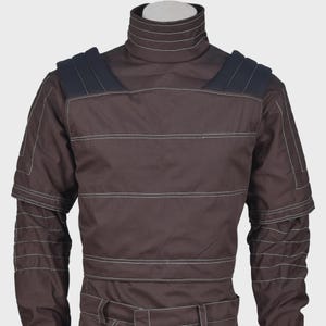 K&ouml;nnte beinhalten: Ein dunkelbraunes Langarmshirt mit hohem Stehkragen, horizontalen wei&szlig;en Ziern&auml;hten und dunkelblauen Schulterpartien. Das Kleidungsst&uuml;ck verf&uuml;gt &uuml;ber strukturierte Details an den &Auml;rmeln sowie einen Bund mit G&uuml;rtelschlaufen.